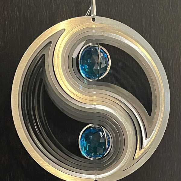 Metal wind chime with blue and clear crystal accents hanging on a dark surface