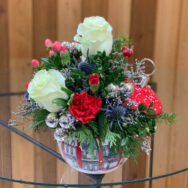 Holiday floral arrangement in a red ornament-shaped container with white roses and red carnations