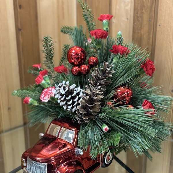 Holiday arrangement in a red toy truck with pine, pinecones, and red accents