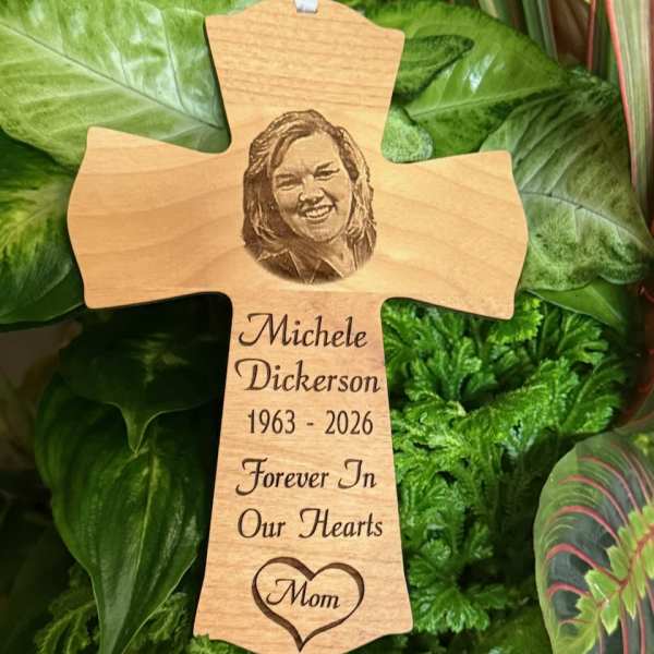 Wooden memorial cross with engraved portrait and text among green foliage