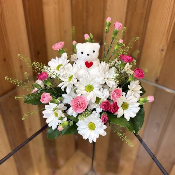 White daisies and pink carnations with a small teddy bear centerpiece