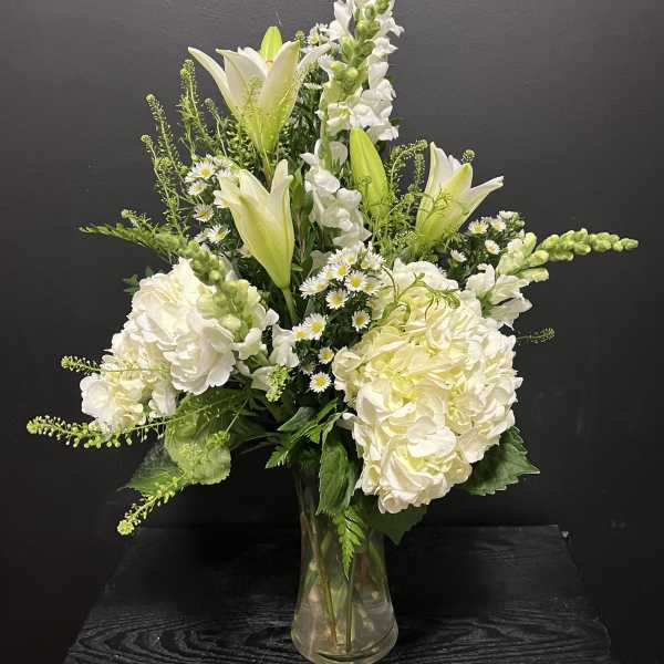 White lilies and hydrangeas arranged in a clear glass vase