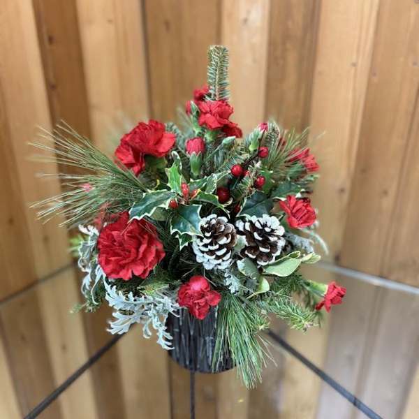 Holiday arrangement with red carnations, pinecones, and evergreen in a black container