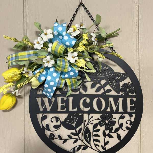 Floral welcome sign with yellow and white flowers and blue ribbons