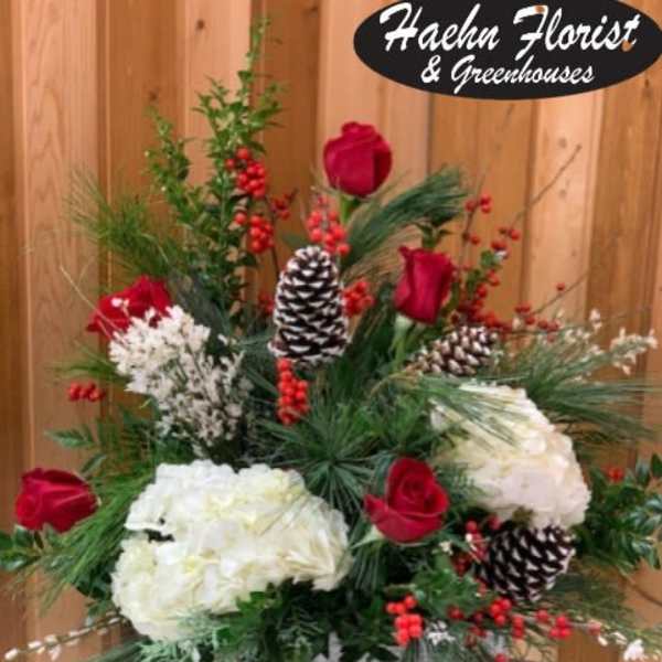 Holiday floral arrangement with red roses, white blooms, pinecones, and berries