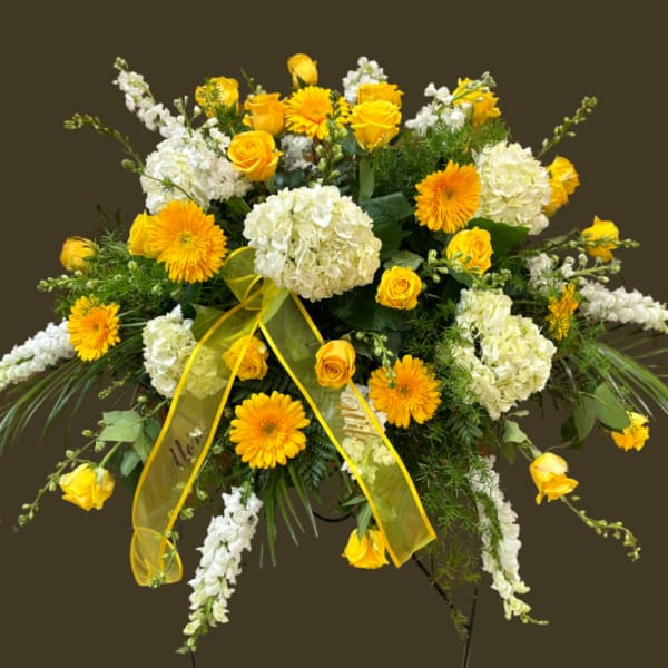 Yellow roses and white hydrangeas in a large standing spray with a yellow ribbon
