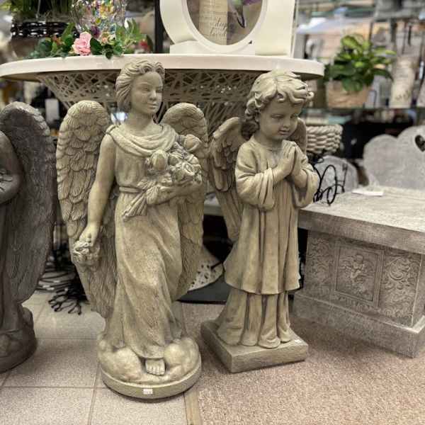 Three angel statues displayed in a store, with a small floral arrangement on a table behind them.