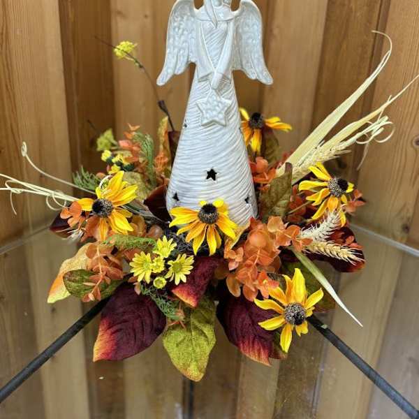 Angel figurine surrounded by yellow and orange flowers in an autumn arrangement