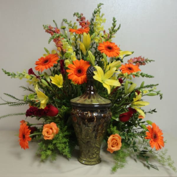 Orange gerbera daisies and yellow lilies in a decorative vase