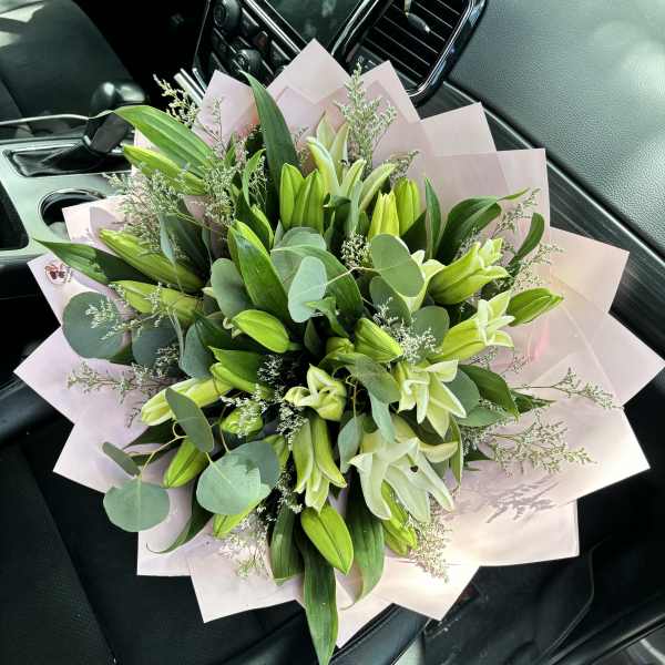 Bouquet of pale lilies and greenery wrapped in pink paper
