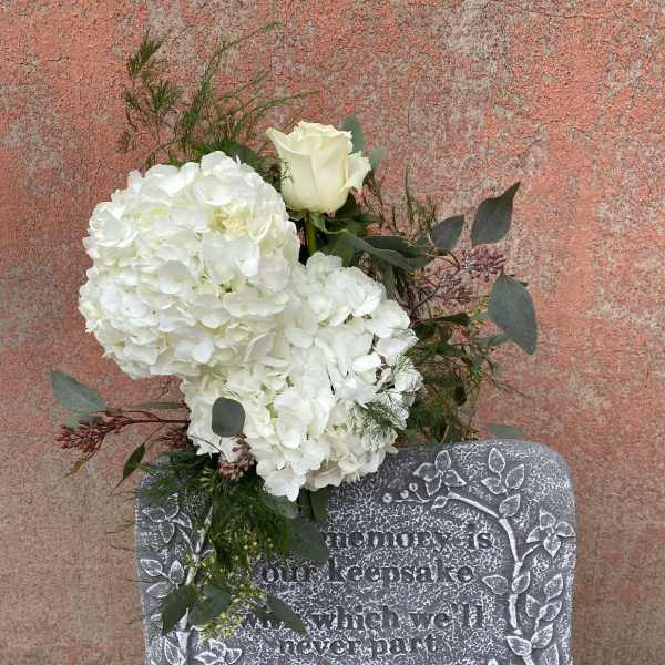 White floral spray on a memorial stone with a single white rose