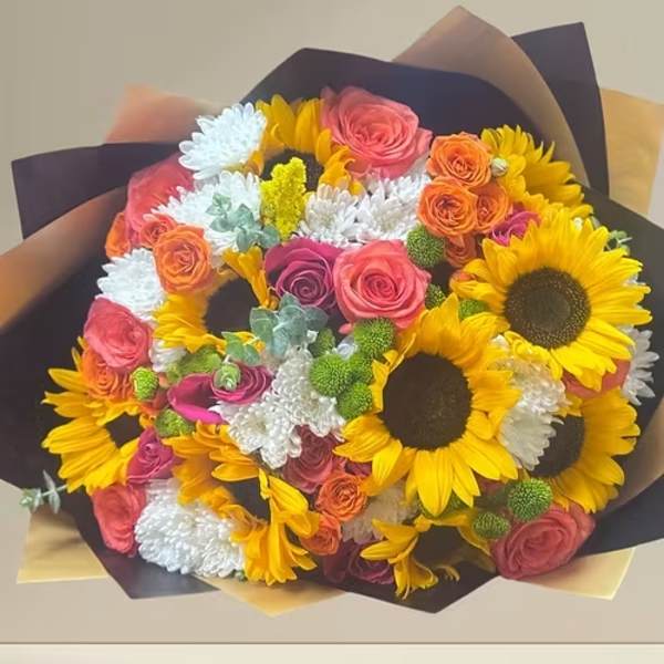 Bouquet of sunflowers, roses, and white daisies wrapped in dark paper