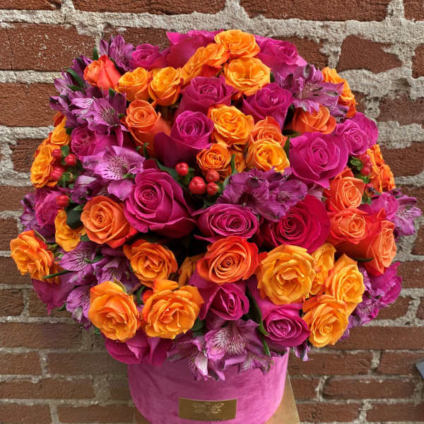 Round bouquet of pink, orange, and purple roses in a pink hat box