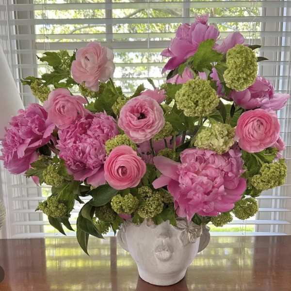 Pink floral arrangement in a white face-shaped vase