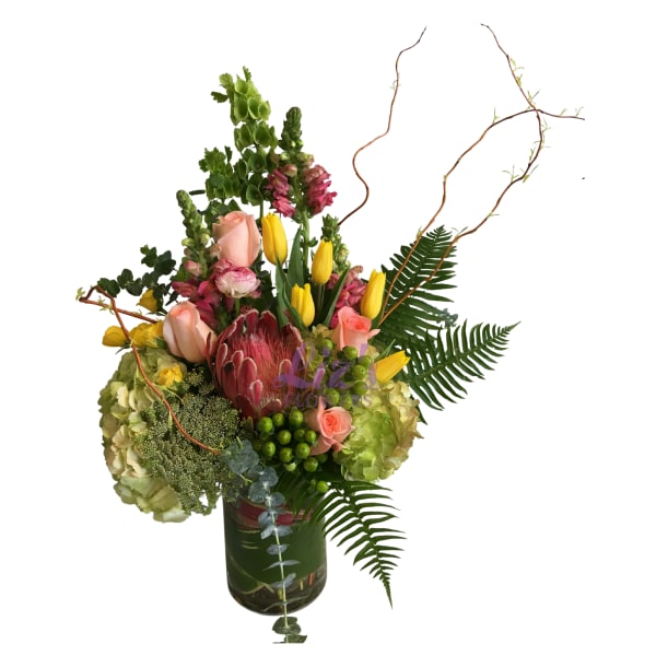 Mixed bouquet with pink roses, yellow tulips, and a protea in a glass vase