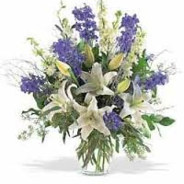 White lilies and purple flowers in a clear glass vase