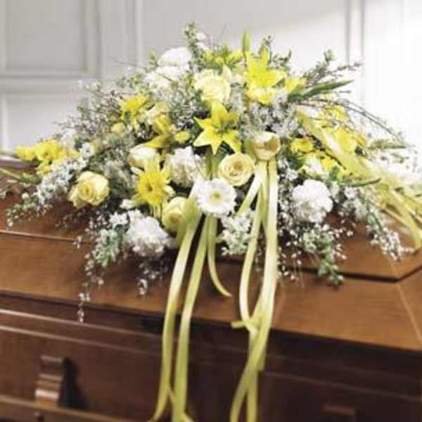 Yellow and white floral spray on a casket with long ribbon streamers
