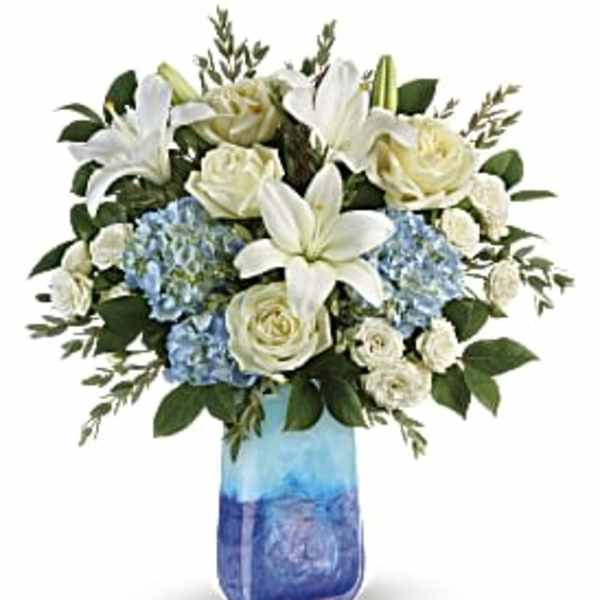 White lilies, roses, and blue hydrangeas in a blue glass vase