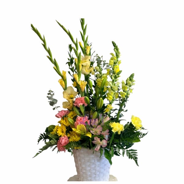 Tall mixed flower arrangement in a white woven basket with yellow and pink blooms