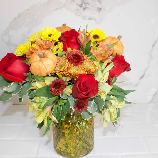 Bouquet of red roses, yellow mums, and pumpkins in a glass vase