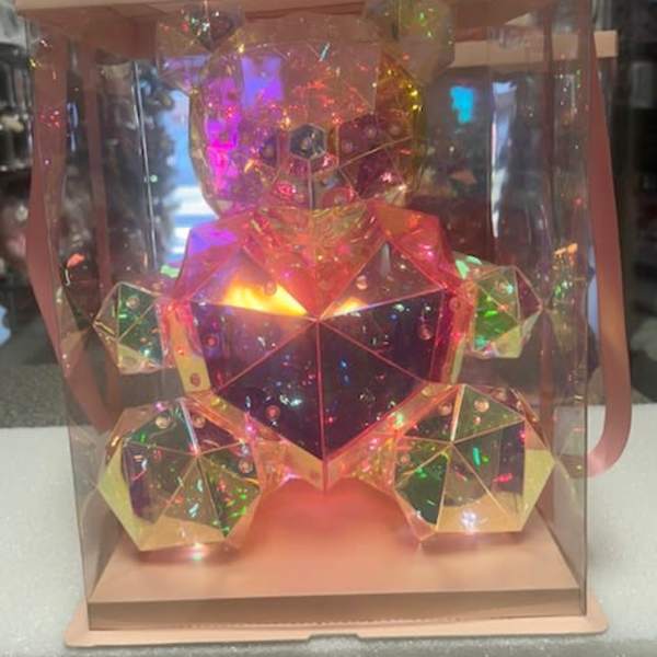 A faceted iridescent teddy bear in a clear gift box with a pink ribbon