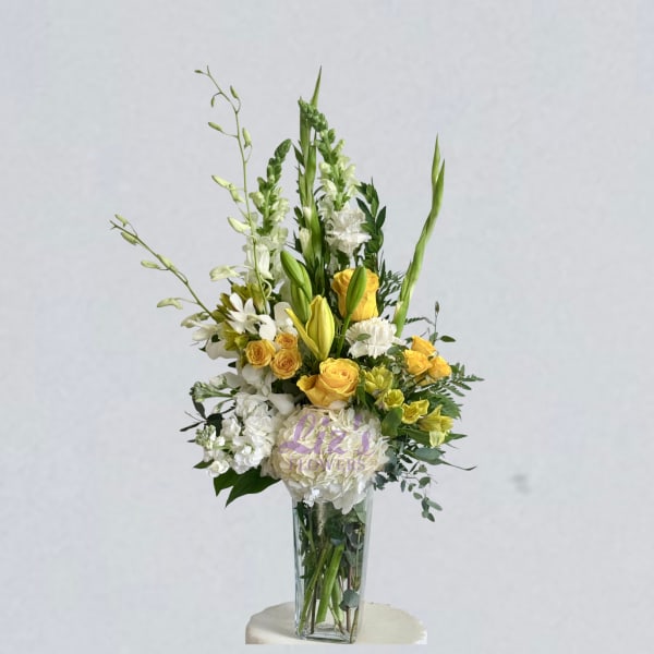 Tall bouquet of yellow and white flowers in a clear glass vase