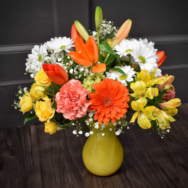 Colorful mixed bouquet in a yellow vase with daisies, roses, and lilies