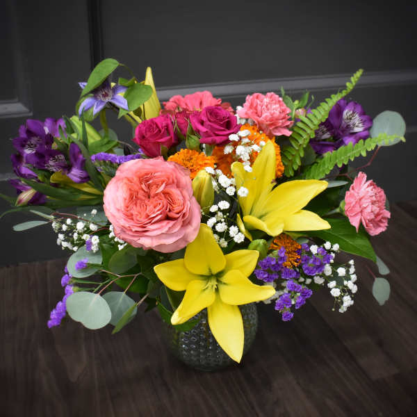 Mixed bouquet with pink roses, yellow lilies, and purple flowers in a vase