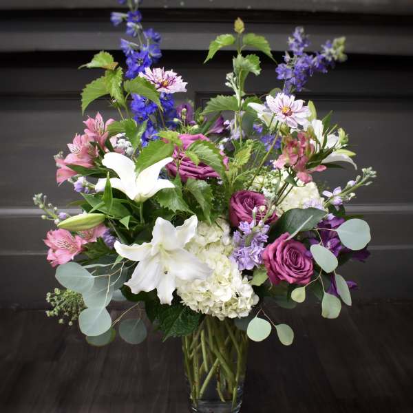 Mixed bouquet of white lilies, purple roses, and pink flowers in a glass vase