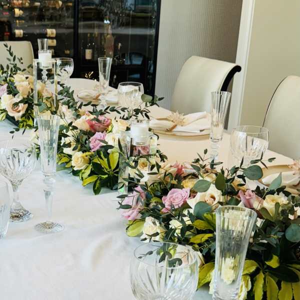 Floral garlands with pink and cream roses on a banquet table with glassware