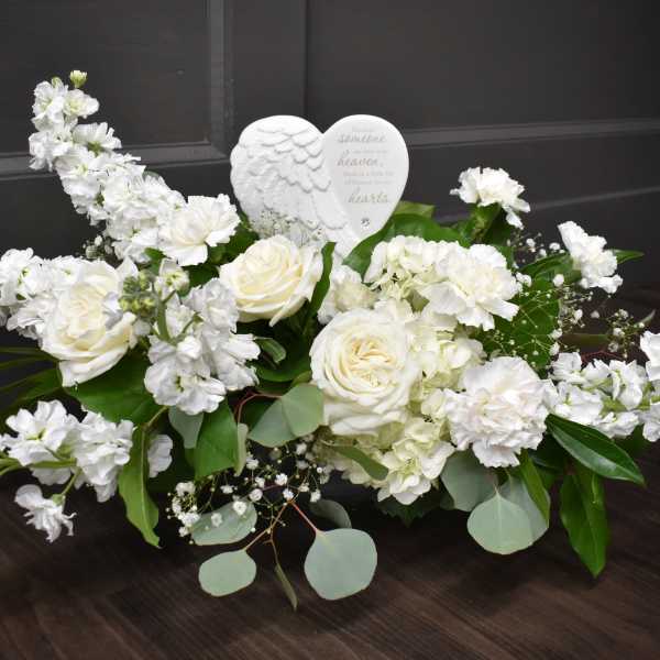 White floral arrangement with roses and carnations around a heart ornament