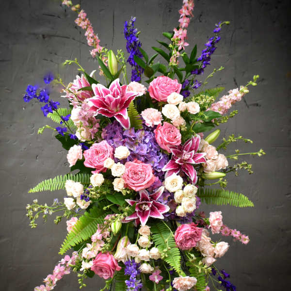 Tall floral spray with pink roses, lilies, and purple blooms on a stand