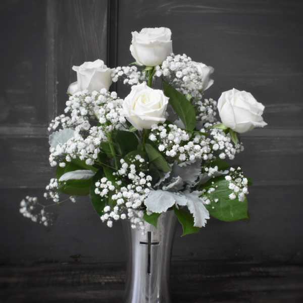 White roses and baby's breath in a silver vase with a cross
