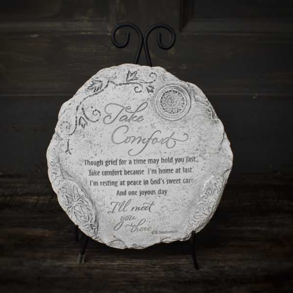 Round decorative plaque on a black stand with the words "Take Comfort"
