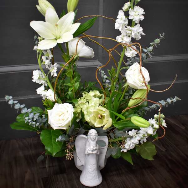 White lilies and roses arranged with greenery in a white angel vase