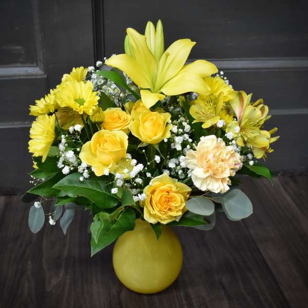Yellow roses and lilies arranged in a yellow vase
