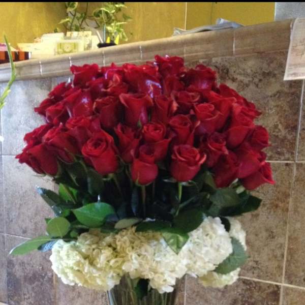 Tall vase arrangement of red roses with white hydrangeas