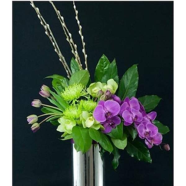 Purple orchids and green flowers in a tall silver vase