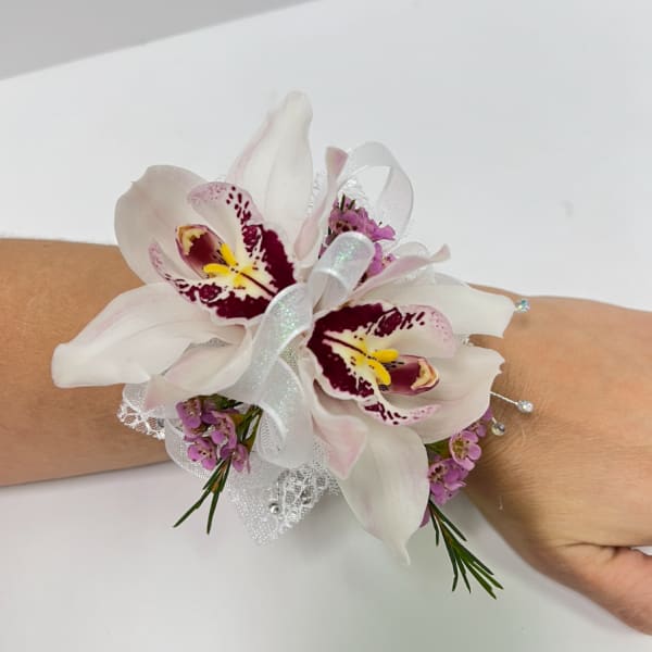 Wrist corsage with two white orchids, pink accents, and white ribbon on an arm
