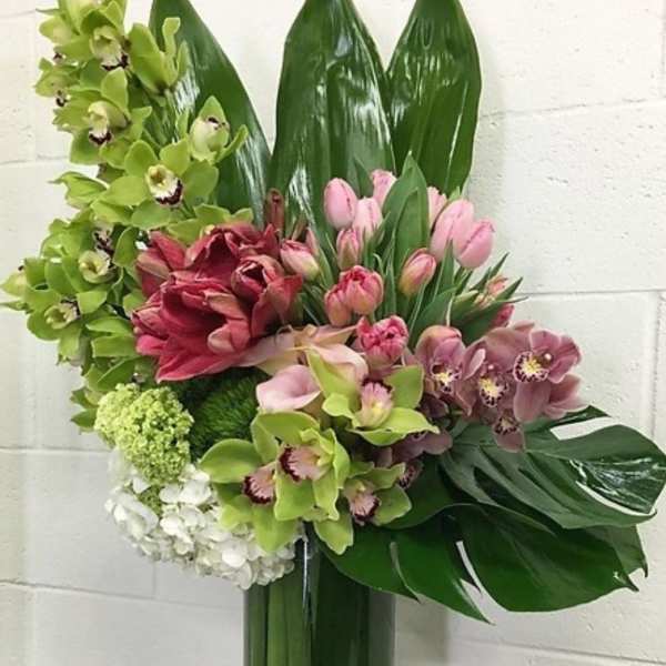 Tall floral arrangement with orchids, tulips, and lilies in a glass vase