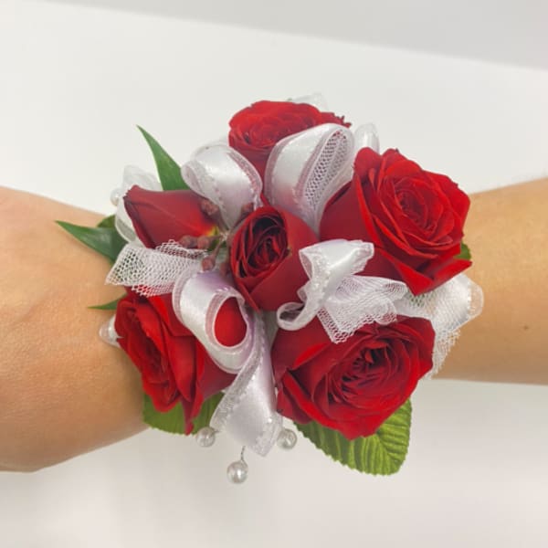Wrist corsage of red roses with white ribbon accents on a person's arm.