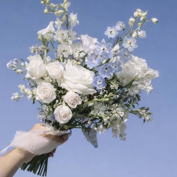 Handheld bouquet of white and pale blue flowers against a blue sky