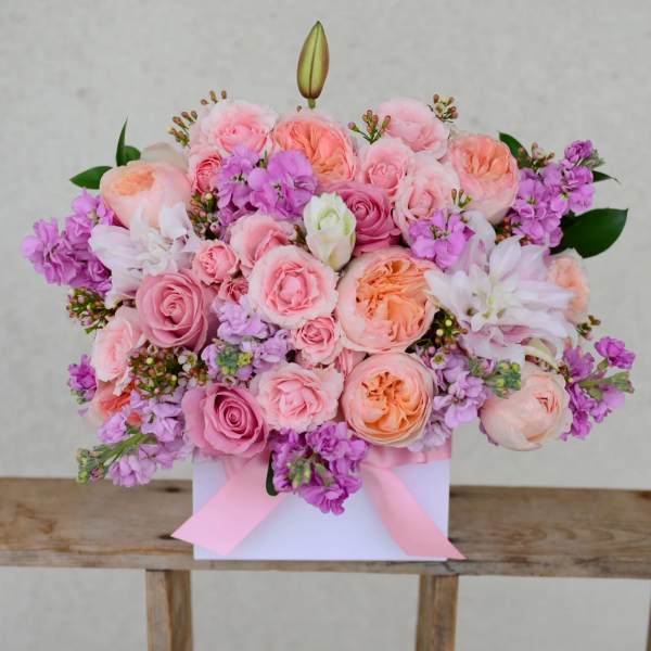 Pink and peach rose bouquet with purple blooms in a white box tied with ribbon