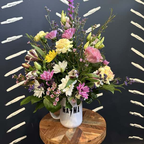 Mixed pastel bouquet in a white mug vase on a wooden stool