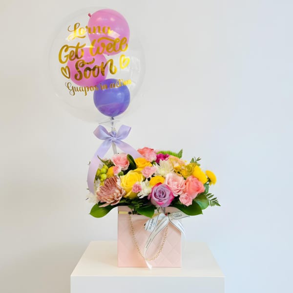 Pink and yellow flower arrangement with a clear balloon reading "Get Well Soon"