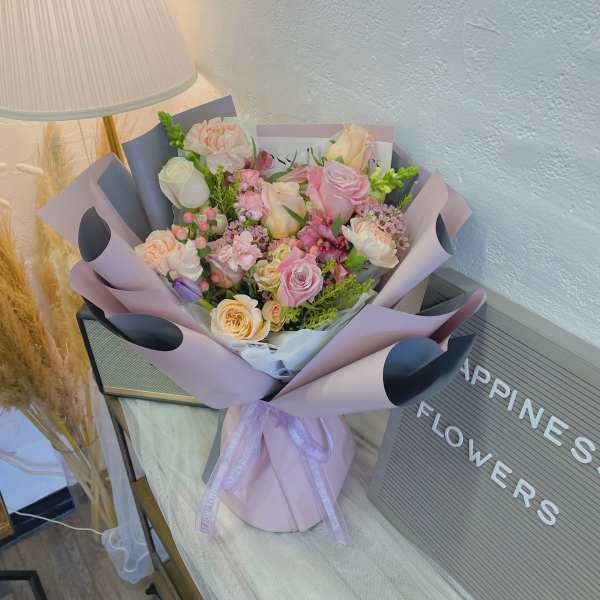 Pastel bouquet of pink and peach roses with mixed blooms in lavender wrap