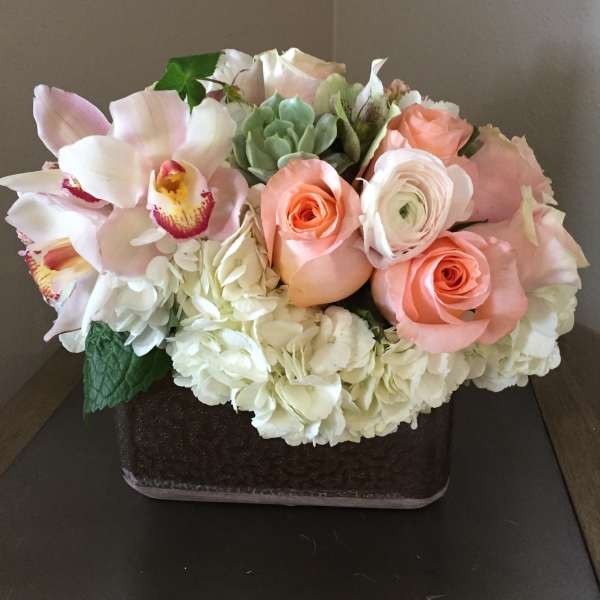 Pastel bouquet with roses, orchids, hydrangeas, and a succulent in a square vase