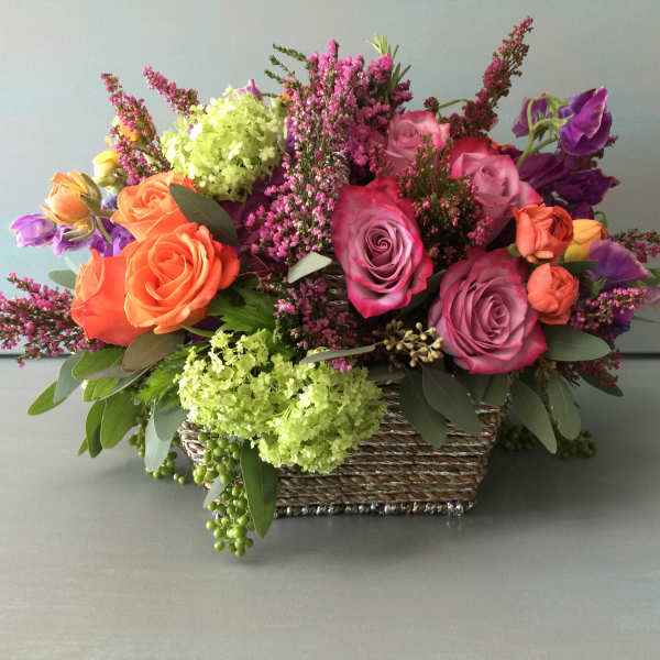 Mixed bouquet of roses and purple flowers in a woven basket