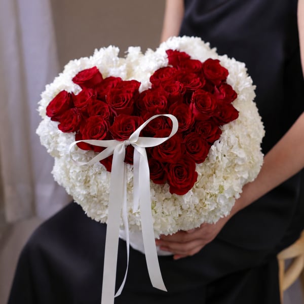 Heart-shaped bouquet of red roses and white flowers with a white ribbon