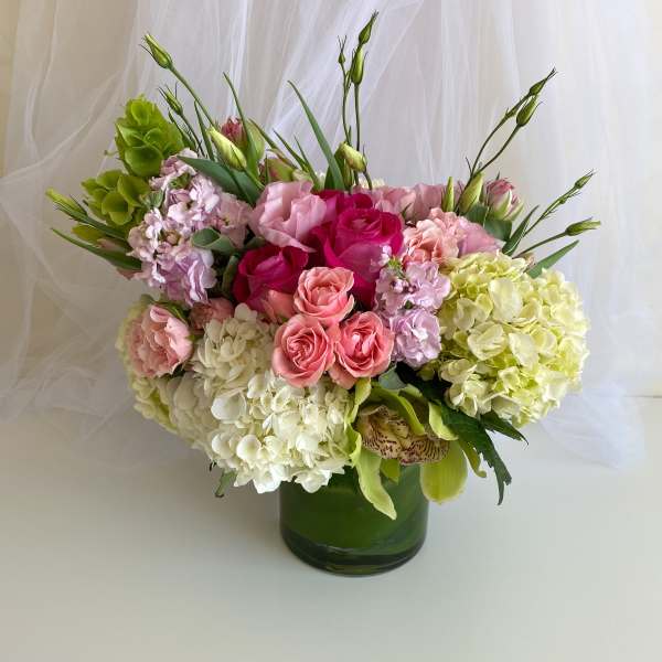 Pink and white floral arrangement in a green glass vase